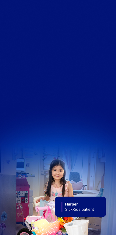 Harper at SickKids, smiling beside her decorated pink bike in her hospital room.