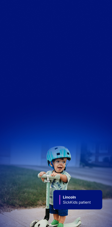 Lincoln outside, smiling while riding his scooter and wearing a helmet.