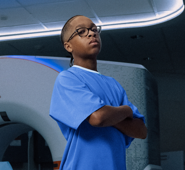 Daniel standing in front of an MRI machine at SickKids with his arms crossed.