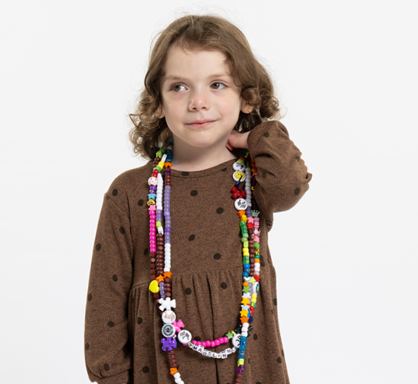 A portrait of Madelynn on a white backdrop. She is looking off camera and wearing strands of colourful bravery beads. 
