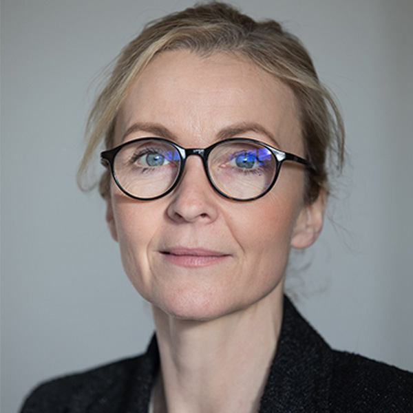 Dr. Louise Gallagher, child psychiatrist and chief of Child and Youth Mental Health at SickKids and CAMH, poses in front of a neutral background. She has blond hair pulled back from her face, has on dark, round glasses and is wearing a dark blazer. 